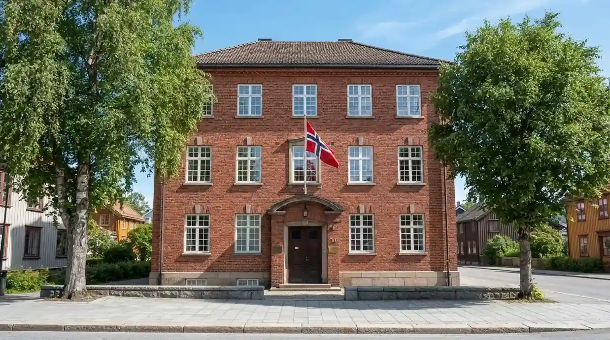 Offentlig kontorbygning i rødt murstein i en norsk by, med et flagg ved inngangen og blå himmel